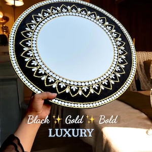May include: Round mirror with a black, gold, and white decorative border. The border features a repeating floral pattern and a beaded edge. The text "Black Gold Bold LUXURY" is at the bottom.