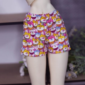 May include: Pink shorts with a cartoon dog print. The dogs are wearing different colored hats and have different expressions.