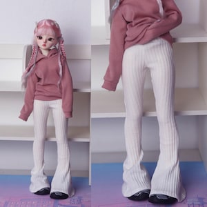 May include: A doll wearing a pink hoodie and white ribbed flare pants. The doll has long pink hair and blue eyes.