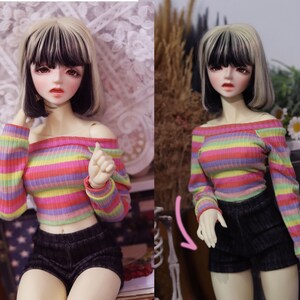 May include: A doll wearing a rainbow striped off-the-shoulder crop top with long sleeves and black shorts.