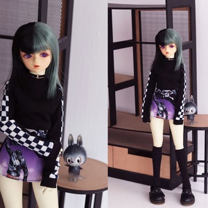 May include: A doll with black and green hair wearing a black and white checkered long-sleeved shirt, a purple and black skirt with a graphic print, and black knee-high socks. The doll is standing on a wooden floor.