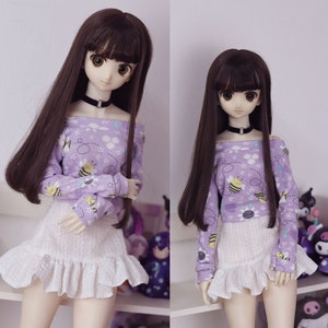 May include: Two dolls with long brown hair and large eyes. They wear a black choker, a light purple off-the-shoulder top with a bee and flower pattern, and a white ruffled skirt. The dolls are posed in front of a white background.