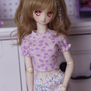 May include: A doll with long brown hair in pigtails wearing a pink and purple floral crop top and matching floral shorts.