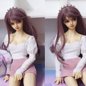 May include: A doll with long purple hair wearing a white, ruffled, long-sleeved blouse and a pink skirt. The doll is wearing a silver headband with rhinestones.