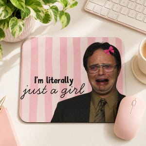 May include: Mouse mat with a pink and white striped background, featuring a crying man with a pink bow. The text "I'm literally just a girl" is printed on the mat. A pink mouse is next to the mat.