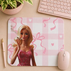 May include: A pink mousepad with a Barbie doll illustration smoking a cigarette. The background features a pink and white gingham pattern with pink ribbons and hearts. A pink mouse, keyboard, and pen are also visible.