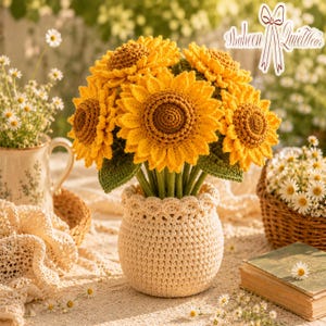 May include: A handcrafted bouquet of yellow crochet sunflowers in a beige crochet vase. The sunflowers have brown centers and green leaves. The vase sits on a table with other decorative items, including a basket of daisies and a vintage book. The image includes the text "Shaheen QuietWear".