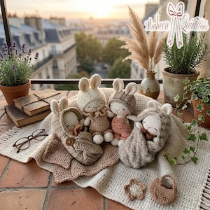 Op de afbeelding: Een verzameling handgemaakte gehaakte konijnenpoppen in verschillende tinten beige, bruin en roze. De poppen zijn gerangschikt op een crèmekleurige deken, met gehaakte babyschoentjes en een kleine gehaakte handtas. De achtergrond bevat planten en een stadsgezicht.