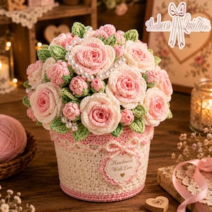 May include: A handcrafted crochet flower arrangement in a decorative pot. The bouquet features pink and white roses, green leaves, and pearl accents. The pot is cream-colored with pink trim and the words "Handmade With Love".