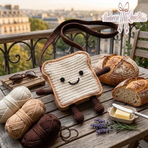 Puede incluir: Un bolso de crochet hecho a mano con forma de rebanada de pan tostado con una cara sonriente, correa marrón, brazos y piernas. Sobre una mesa de madera con hilo, gafas de sol, pan y mantequilla. El fondo muestra una vista de la ciudad.