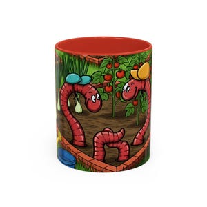 May include: A ceramic coffee mug with a red interior and a wrap-around cartoon design. The design features three red worms in a garden setting with tomatoes and onions. The worms are wearing hats and smiling. A blue bucket and yellow watering can are also visible.