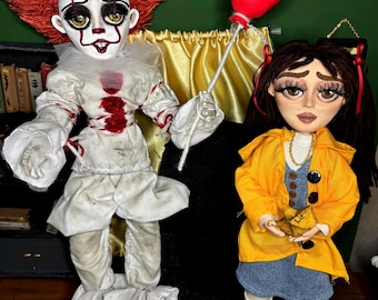 May include: Two handmade dolls: one is a clown with red hair and a white costume, holding a red balloon. The other doll is a girl in a yellow jacket and denim dress. The clown doll has red accents and the girl doll has a gold necklace.