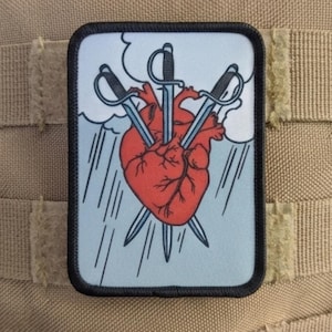 Könnte beinhalten: Ein rechteckiger Aufnäher mit einem roten Herzen, das von drei Schwertern durchbohrt wird. Das Design umfasst einen hellblauen Hintergrund mit Regen und Wolken sowie einen schwarzen Rand. Der Aufnäher ist auf einem beigefarbenen Stoff angebracht.