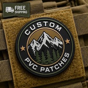 Peut inclure: Un écusson circulaire en PVC représentant une chaîne de montagnes aux sommets enneigés blancs au-dessus d'une forêt de pins verts. La bordure noire porte le texte blanc CUSTOM PVC PATCHES et deux étoiles dorées sur un tissu beige.