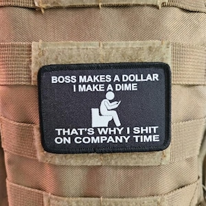 May include: A rectangular black morale patch with white embroidered text that reads BOSS MAKES A DOLLAR I MAKE A DIME THAT'S WHY I SHIT ON COMPANY TIME, featuring a white graphic of a stick figure sitting on a toilet while looking at a phone.