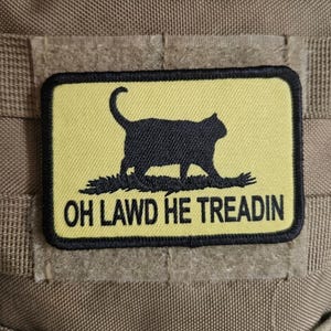 Op de afbeelding: Een rechthoekige patch met een zwart katten silhouet op een gele achtergrond. De tekst "OH LAWD HE TREADIN" is eronder in het zwart gedrukt. De patch is zwart omrand en heeft een klittenband achterkant.