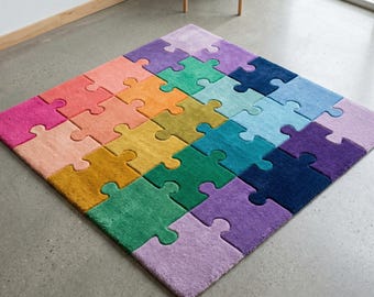 May include: A colorful puzzle-piece rug with a variety of colors, including pink, orange, yellow, green, blue, and purple. The rug is made up of individual puzzle pieces, creating a unique and playful design. The rug is placed on a gray concrete floor.