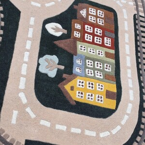 Soft Montessori kids rug designed with a realistic transportation town featuring looping railway tracks, paved roads, schoolhouse, colorful residential buildings, elegant home, green trees, landscaped parks, roundabout, and waterfront sailboat scene. Positioned beneath a modern dining table, this interactive play rug creates an engaging environment where children can build stories, navigate toy vehicles, and develop essential early learning skills.