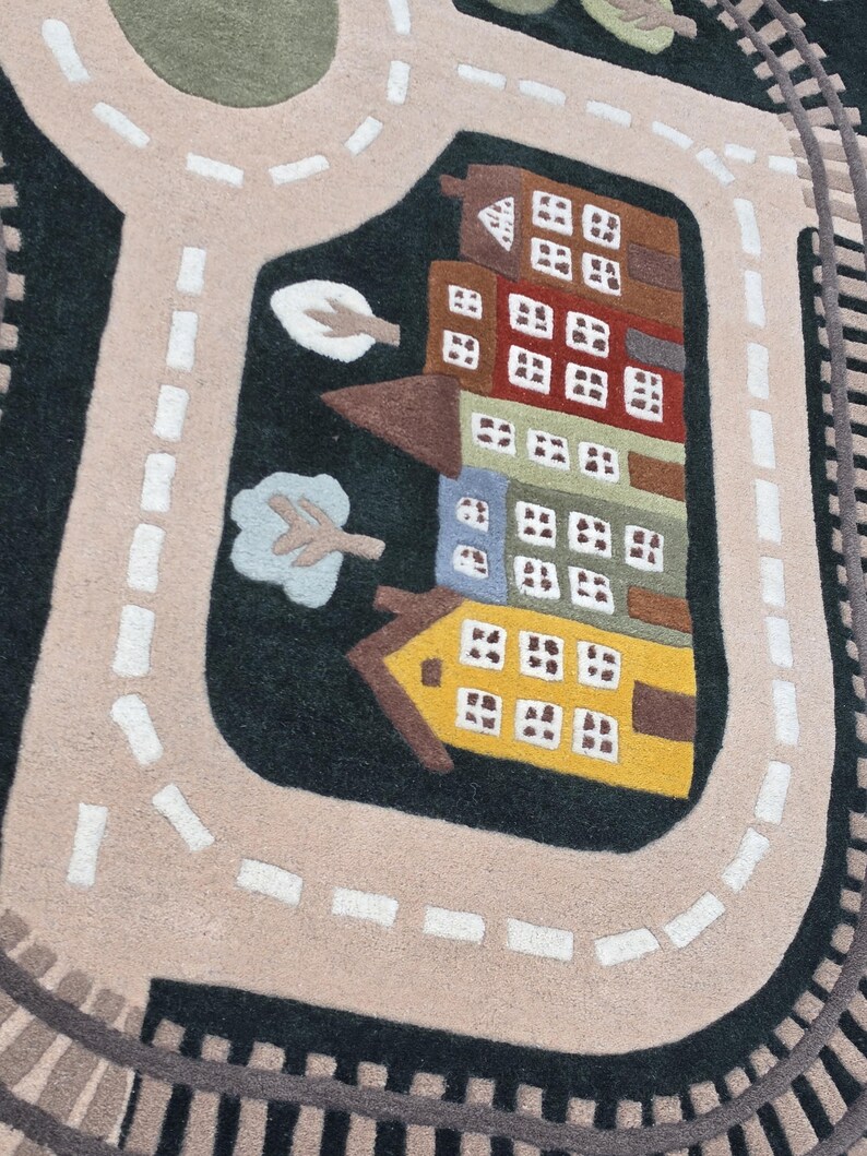 Soft Montessori kids rug designed with a realistic transportation town featuring looping railway tracks, paved roads, schoolhouse, colorful residential buildings, elegant home, green trees, landscaped parks, roundabout, and waterfront sailboat scene. Positioned beneath a modern dining table, this interactive play rug creates an engaging environment where children can build stories, navigate toy vehicles, and develop essential early learning skills.