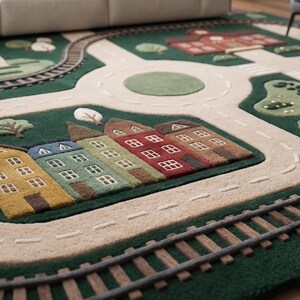 Large Kids Playroom Rug designed with an interactive town map including roads, train tracks, school, neighborhood buildings, roundabout, lake, trees, and sailboat for imaginative educational play. This plush children's rug supports creativity, motor skill development, storytelling, and pretend transportation games using toy cars and wooden trains. Suitable for Montessori classrooms, homeschool activities, daycare facilities, nurseries, and modern kids' bedrooms.