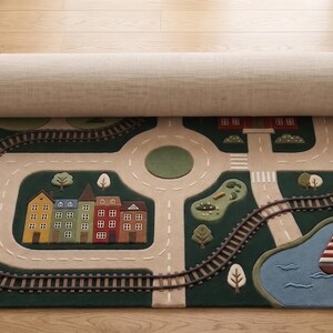 Interactive City Play Rug with train tracks, winding roads, school, neighborhood homes, landscaped greenery, roundabout, lake, and sailboat creates an exciting learning environment for toddlers and young children. Designed for imaginative storytelling, this children's activity rug supports educational play with toy trains, wooden vehicles, and miniature figures.