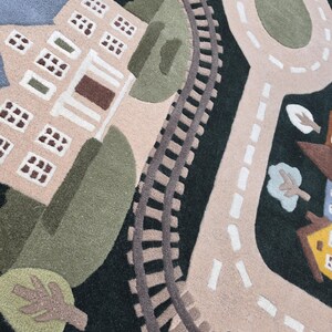 Children's railway and road map rug featuring a beautifully illustrated town with detailed train tracks, curved streets, school building, residential neighborhood, central roundabout, landscaped trees, and a blue lake with sailboat. Displayed in a bright contemporary dining room, this soft educational rug blends luxury home décor with child-friendly functionality.