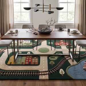 Modern kids play rug featuring an interactive miniature town with winding roads, realistic railway tracks, a neighborhood school, colorful residential houses, a large family home, landscaped trees, a scenic blue lake with a sailboat, and a central roundabout. Displayed beneath a contemporary wooden dining table in a bright, minimalist home, this educational area rug combines imaginative play with stylish interior design.