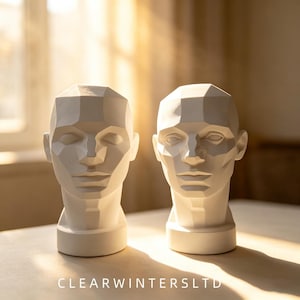 May include: Two white, geometric, faceted head sculptures featuring angular planes and sharp lines. Each bust displays a stylized human face with defined features, including eyes, a nose, and lips, set on a cylindrical base. Text reads CLEARWINTERSLTD.