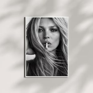 May include: Black and white portrait print of a woman with long, flowing hair, holding a cigarette in her mouth. The image is framed in a white border, with a soft, neutral background. The photograph is a close-up, focusing on the woman's face.
