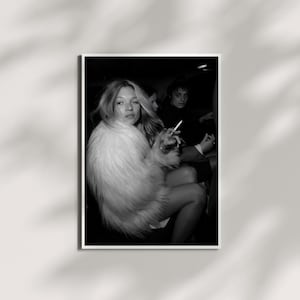 May include: Monochrome photograph featuring a woman in a fluffy white coat, holding a cigarette. Two other individuals are partially visible in the background. The image is a portrait, with the woman looking towards the camera.