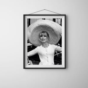 K&ouml;nnte beinhalten: Gerahmter Schwarz-Wei&szlig;-Druck einer Frau mit gro&szlig;em Sonnenhut. Sie tr&auml;gt eine hellfarbene Jacke mit Kn&ouml;pfen. Das Bild ist ein Portr&auml;t mit verschwommenem Hintergrund.