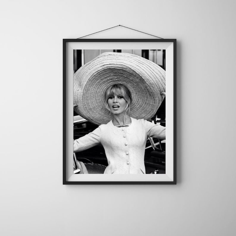 K&ouml;nnte beinhalten: Gerahmter Schwarz-Wei&szlig;-Druck einer Frau mit gro&szlig;em Sonnenhut. Sie tr&auml;gt eine hellfarbene Jacke mit Kn&ouml;pfen. Das Bild ist ein Portr&auml;t mit verschwommenem Hintergrund.