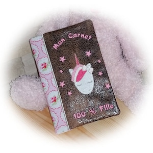 以下が含まれることがあります： ユニコーンのデザインと「Mon Carnet 100％Fille」というテキストが書かれた、茶色とピンクのノートブックです。