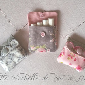 May include: Three small fabric pouches with floral patterns and buttons. The pouches are closed and have a scalloped edge. The text "Petite Pochette de Sac à Marin" is written below the pouches.