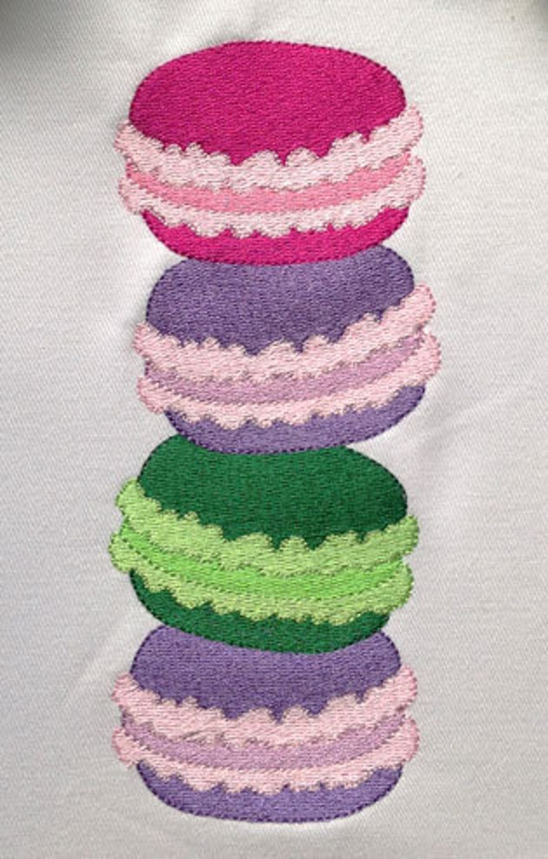 May include: A stack of four colorful macarons with pink, purple, green, and purple frosting. The macarons are arranged vertically, with the pink macaron on top and the purple macaron on the bottom.