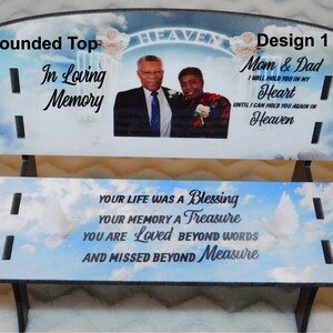 May include: A memorial bench with a rounded top, featuring a photo of a couple and the text "In Loving Memory." The bench has a sky and cloud background with doves and the words "Your Life Was a Blessing."