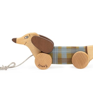 May include: A wooden toy dachshund with a plaid pattern on its body. The toy has wheels and a rope attached to it, making it a pull toy. The toy is labelled "remarkable" on the bottom.