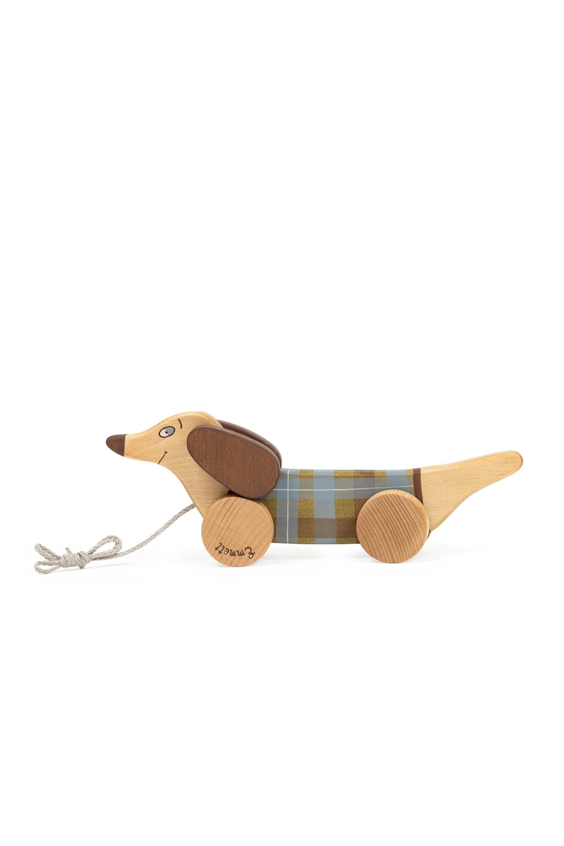 Puede incluir: Un juguete de madera en forma de dachshund con un patr&oacute;n de cuadros en su cuerpo. El juguete tiene ruedas y una cuerda atada a &eacute;l, lo que lo convierte en un juguete de arrastre. El juguete est&aacute; etiquetado como "remarkable" en la parte inferior.