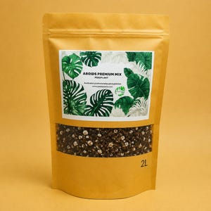 Puede incluir: Una bolsa vertical de color canela que contiene 2L de sustrato Aroids Premium Mix. La etiqueta presenta ilustraciones de hojas de monstera verdes y el texto AROIDS PREMIUM MIX PEKEPLANT. Una ventana transparente muestra la tierra y perlita.