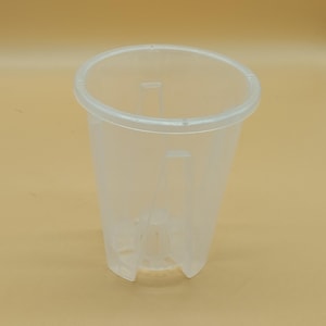 Può includere: Un vaso di plastica trasparente con una parte superiore ampia e rotonda e un corpo affusolato. Il vaso ha dei supporti verticali all'interno e dei fori di drenaggio sul fondo. Il vaso è progettato per piantare fiori o altre piante.