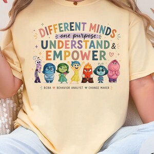 Könnte beinhalten: Ein buttergelbes Kurzarm-T-Shirt mit einem Grafikdruck mit dem Text "DIFFERENT MINDS one purpose UNDERSTAND & EMPOWER" über Illustrationen von sieben bunten Zeichentrickfiguren und dem Text "BCBA BEHAVIOR ANALYST CHANGE MAKER".