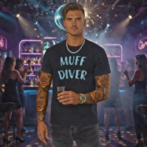 May include: A black t-shirt with the words "MUFF DIVER" in light blue. The person in the image has rose tattoos on their arms and is holding a glass of liquid. They are wearing a silver chain and a watch.