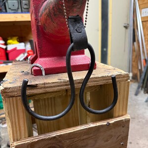 May include: A red anvil with a black metal hook attached by a leather strap and chain. The anvil is mounted on a wooden stand. The hook is in the shape of a double S.