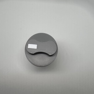 Peut inclure: Un bouchon de bouteille gris avec une poignée incurvée et un accent argenté rectangulaire. Le bouchon est circulaire et a une surface texturée. La poignée est d'une nuance de gris plus foncée.