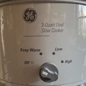 May include: A white 3-Quart oval slow cooker with a GE logo. The control dial has settings for Keep Warm, Low, and High. The slow cooker is designed for convenient cooking.