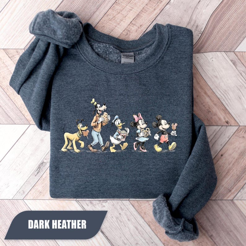 May include: Dark heather gray sweatshirt featuring a graphic of Disney characters Pluto, Goofy, Donald Duck, Minnie Mouse, and Mickey Mouse. The characters are holding food items. The text "DARK HEATHER" is at the bottom of the image.
