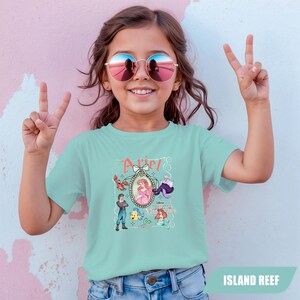 Puede incluir: Una camiseta azul claro con un gr&aacute;fico de Ariel de La Sirenita. El gr&aacute;fico incluye a Ariel, el Pr&iacute;ncipe Eric, Flounder, Sebasti&aacute;n y &Uacute;rsula. La palabra "Ariel" est&aacute; escrita encima del gr&aacute;fico en una fuente decorativa. La camiseta la lleva una ni&ntilde;a.