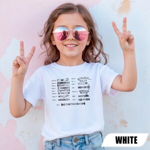 May include: A white t-shirt featuring a schematic diagram of various lightsabers. The shirt is worn by a young person wearing round sunglasses and making a peace sign with their fingers. The word "WHITE" is printed at the bottom of the image.