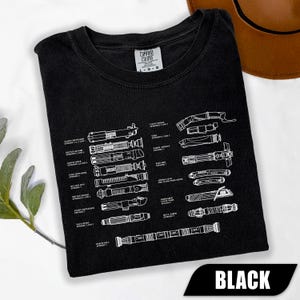 May include: Black t-shirt with a white diagram of various lightsabers from a popular science fiction franchise. The shirt includes the text "BLACK" in a white font on a black banner.