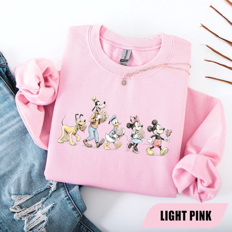 May include: Light pink sweatshirt featuring a graphic of Disney characters: Pluto, Goofy, Donald Duck, Minnie Mouse, and Mickey Mouse. The characters are walking and holding food items. The text "LIGHT PINK" is at the bottom of the image.